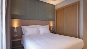 A hotel room with a bed, bedside lamps, a wooden wardrobe, and a patterned wall.