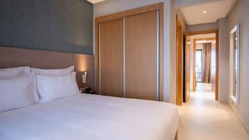 A hotel room with a large bed, a wardrobe, a bedside table with a lamp, and a view of the hallway.