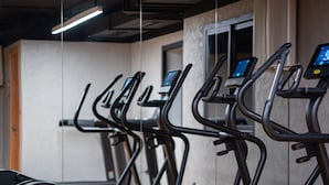 A gym with treadmills and a stationary bike, with a wooden floor and a mirror on the wall.