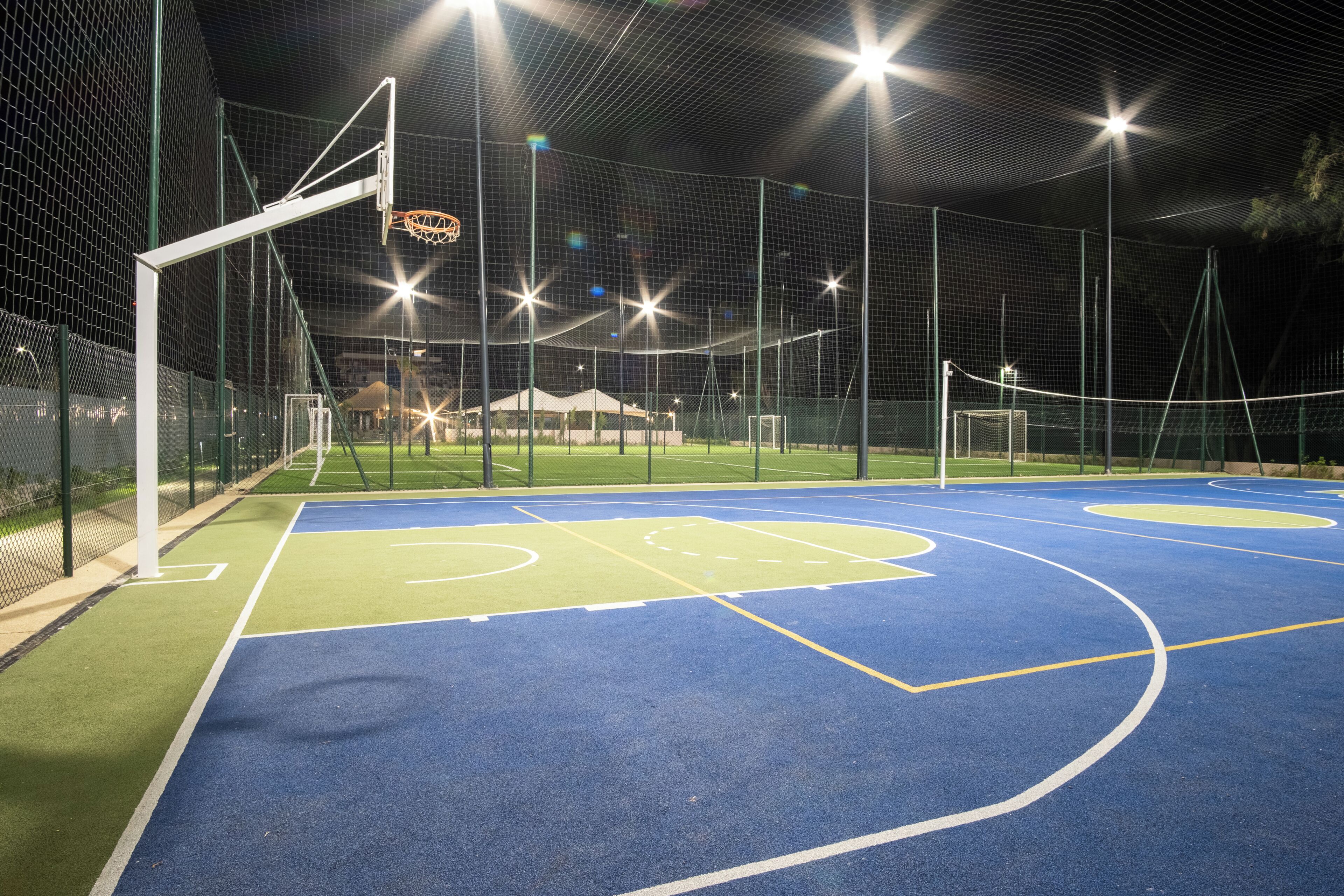 An outdoor basketball court with a net, goalpost, and a fence.