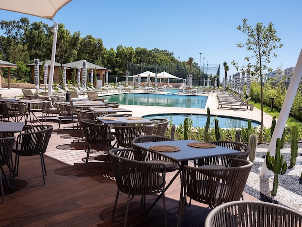 A poolside area with lounge chairs, tables, and a pool.