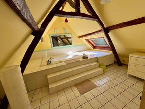 Ein kleines, dreieckiges Schlafzimmer im Dachgeschoss mit freistehender Badewanne, einem Fenster und einem kleinen Spiegel.