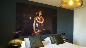Une chambre d’hôtel avec un grand lit, deux tables de chevet, une lampe fixée au mur et un tableau au-dessus du lit.