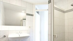 A bathroom with white tiles, a white sink, and a mirror. - Groepsaccommodatie 18 Otterlo (Otterlo)