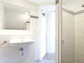 A bathroom with white tiles, a white sink, and a mirror. - Groepsaccommodatie 18 Otterlo (Otterlo)