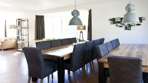 A dining area with a wooden table and black upholstered chairs, a pendant light, and a modern wall art piece. - Groepsaccommodatie 18 Otterlo (Otterlo)