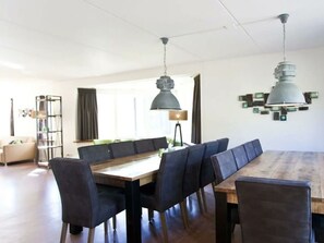 A dining area with a wooden table and black upholstered chairs, a pendant light, and a modern wall art piece. - Groepsaccommodatie 18 Otterlo (Otterlo)