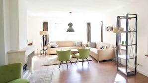A living room with a sofa, two chairs, a floor lamp, a bookshelf, and a fireplace. - Groepsaccommodatie 18 Otterlo (Otterlo)