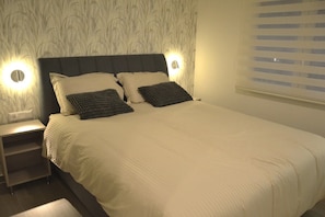 Ein ordentlich bezogenes Bett mit Kopfteil, zwei Nachttischen und einer Wand mit ornamentalem Wandpapier.