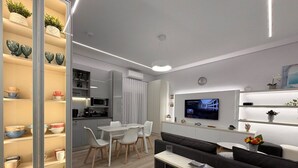 A modern living room with a sofa, TV, and a dining area with chairs and a table. - Flisvos Beach Retreat (ΑΘΗΝΑ)