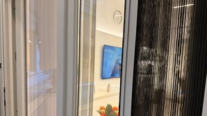 A room with a sliding door, a small round table with a potted plant, a clock on the wall, and a television. - Flisvos Beach Retreat (ΑΘΗΝΑ)