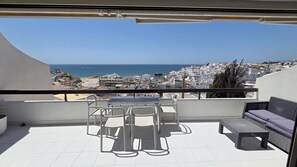 Ein Balkon mit Tisch, Stühlen, einer Sitzecke und Blick auf das Meer und die Gebäude.