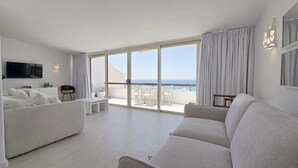 Uma sala de estar moderna com um sofá, uma TV e uma varanda com vista para o mar.
