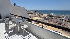 Uma varanda com mesa e cadeiras, com vista para uma cidade costeira e o mar.