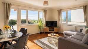 A living room with a TV, sofa, dining table, chairs, and large windows with curtains. - Amazing Location - Free Parking - Beach Opposite! (Bournemouth)