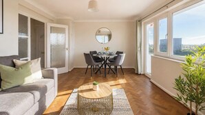 A modern living room with a sofa, dining table, chairs, a round coffee table, and a large window with a view. - Amazing Location - Free Parking - Beach Opposite! (Bournemouth)