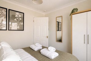 Ein Hotelzimmer mit einem Bett, zwei gerahmten floralen Bildern, einer weißen Tür, einem Spiegel und einem Kleiderschrank.