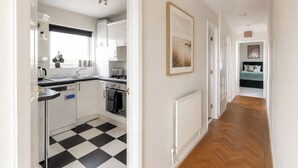 A kitchen with a black and white checkered floor, white cabinets, a radiator, and a hallway leading to a bedroom. - Amazing Location - Free Parking - Beach Opposite! (Bournemouth)