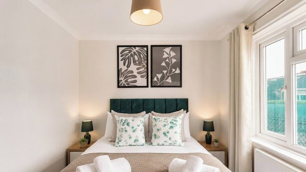 Quarto bem arrumado com uma cama, duas mesas de cabeceira, uma janela com cortinas e duas obras de arte emolduradas na parede.