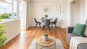 Uma sala de estar moderna com área de jantar, grandes janelas e vista para o exterior.