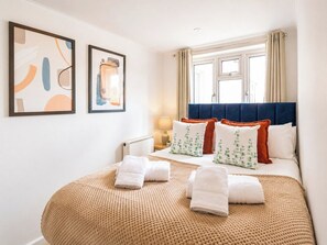 Een hotelkamer met een bed, kussens, een raam met gordijnen en twee kunstwerken in lijsten aan de muur.