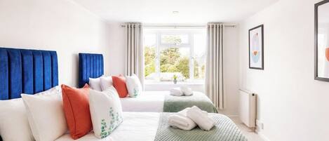 Ein Hotelzimmer mit zwei Betten, einem Fenster mit Vorhängen, einem Heizkörper und einem gerahmten Bild an der Wand.