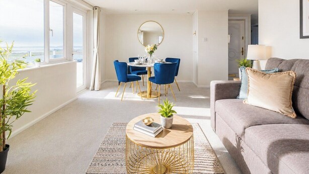Una sala de estar moderna con un sofá, una mesa de centro redonda y un comedor con sillas azules y una mesa blanca.