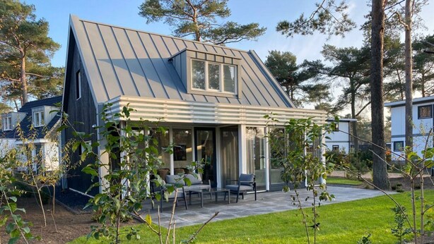 Et moderne hus med skrå metal tag, en overdækket terrasse med havemøbler og en velplejet græsplæne.