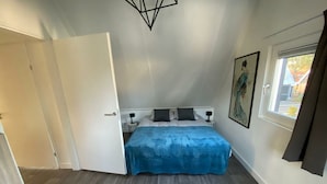 Et soveværelse med seng, et natbord, et vindue med gardiner og en dør.
