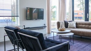En moderne stue med en sofa, to lænestole, et fjernsyn og et lille bord med stearinlys.
