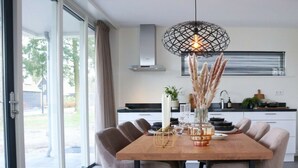 Et moderne spiseområde med et træbord, seks stole, en hængende lampe og udsigt gennem store glasdøre.