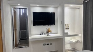 Une chambre d’hôtel moderne dotée d’un grand miroir, d’un téléviseur à écran plat, d’une coiffeuse avec un lavabo et d’un espace douche.