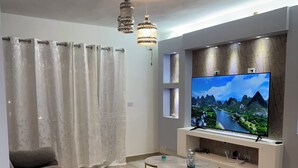 Un salon moderne avec un grand téléviseur à écran plat, un canapé gris, une table basse ronde et un tapis moelleux.