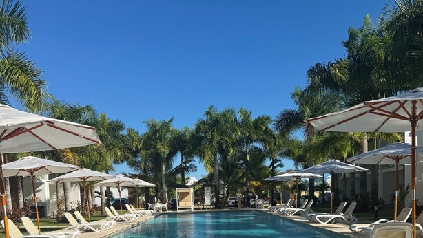 Une piscine entourée de palmiers, avec des chaises longues et des parasols.
