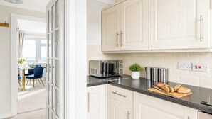 A kitchen with white cabinets, a toaster, a plant, and a cutting board with bread.