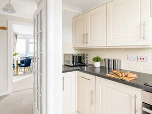 A kitchen with white cabinets, a toaster, a plant, and a cutting board with bread.