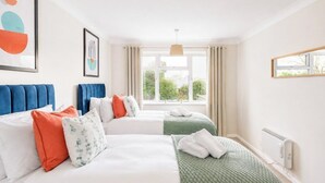 A hotel room with two beds, a window with curtains, a radiator, and artwork on the walls.