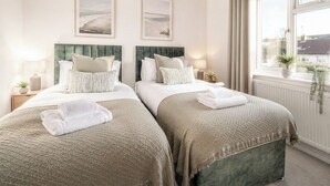 Habitación de hotel con dos camas, una ventana con cortinas, un radiador y cuadros en la pared.