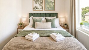 Una cama bien hecha con un cabecero verde, dos mesitas de noche con lámparas y una ventana con cortinas.