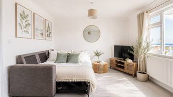 Un dormitorio con cama, televisor, mesita de noche, espejo y ventana con vistas.
