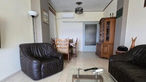 A living room with a glass coffee table, two black leather sofas, a dining table with chairs, a wooden cabinet, and a floor lamp. - Kons Beach Front Apartment with Sea View, Wi-Fi, and Air Conditioning (Kalamata)