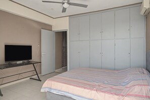 A bedroom with a bed, a television on a stand, a wardrobe, and a ceiling fan. - Kons Beach Front Apartment with Sea View, Wi-Fi, and Air Conditioning (Kalamata)