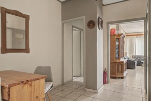A hallway leading to a living area with a dining table, chairs, a sofa, and a cabinet with glass doors. - Kons Beach Front Apartment with Sea View, Wi-Fi, and Air Conditioning (Kalamata)