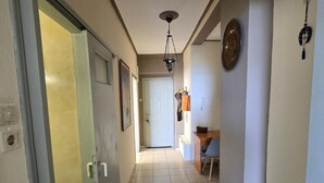 A hallway with a tiled floor, a door on the left, a ceiling light, and a wall-mounted light fixture. - Kons Beach Front Apartment with Sea View, Wi-Fi, and Air Conditioning (Kalamata)