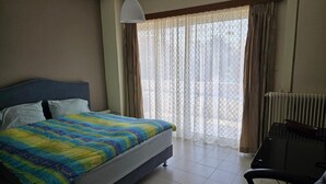 A hotel room with a bed, a chair, a window with curtains, and a radiator. - Kons Beach Front Apartment with Sea View, Wi-Fi, and Air Conditioning (Kalamata)