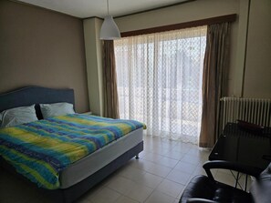 Ein Hotelzimmer mit Bett, Sessel, Fenster mit Vorhängen und Heizkörper.