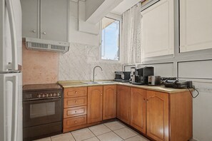 A kitchen with a stove, sink, wooden cabinets, and a window. - Kons Beach Front Apartment with Sea View, Wi-Fi, and Air Conditioning (Kalamata)