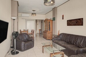 A living room with leather sofas, a glass coffee table, a TV, and a ceiling fan. - Kons Beach Front Apartment with Sea View, Wi-Fi, and Air Conditioning (Kalamata)