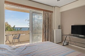 A hotel room with a bed, a TV, a desk, and a balcony with a view of the sea. - Kons Beach Front Apartment with Sea View, Wi-Fi, and Air Conditioning (Kalamata)