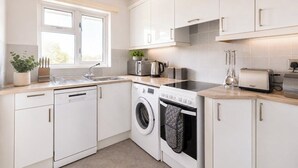 Une cuisine moderne avec des meubles blancs, un lave-vaisselle, une machine à laver, un grille-pain et une bouilloire.